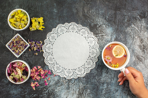 茶俯视图：灰色地面上 一位女士手拿一杯花草茶和几碗花边的干花视图顶部质地