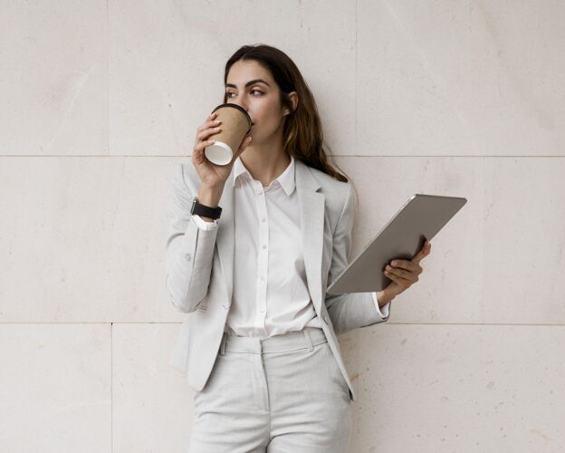 平板电脑优雅的女商人一边喝咖啡一边拿着平板电脑企业家女性时尚