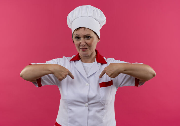 中年身着厨师制服的自信的中年女厨师在孤零零的粉色墙上指着自己的手指手指厨师自信