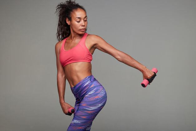 活跃健身年轻苗条的深色皮肤卷曲的女人在粉红色的运动上衣和印刷紧身裤做她的手锻炼摆姿势马尾辫年轻