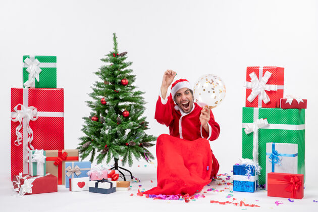 圣诞树圣诞心情与年轻快乐疯狂哈圣诞老人坐在圣诞树和礼物在白色背景上不同的颜色圣诞老人年轻圣诞老人