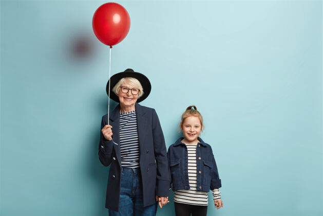 友谊退休老太太的照片牵着可爱的小孙女的手 来派对吧 捧着红气球积极条纹手