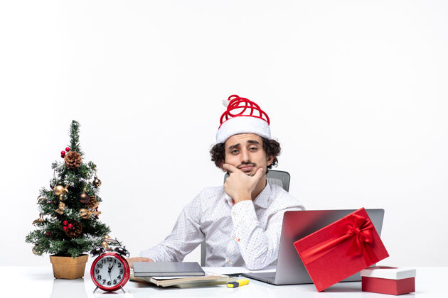 帽子新年心情与脑力激荡的年轻商人与有趣的圣诞老人帽子在白色背景的办公室深思熟虑电脑年轻商人圣诞老人