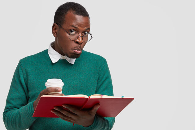 困惑迷糊的黑人男子照片夹着嘴唇 有着迷惑不解的表情 读着考试的必备资料面部咖啡毛衣