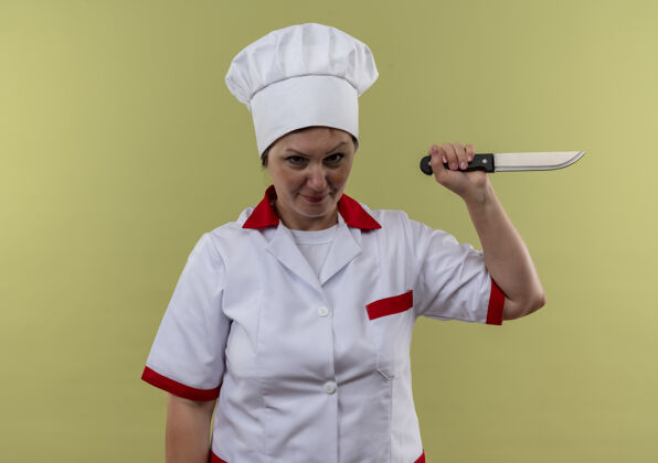 制服身着厨师制服的中年女厨师手持刀站在与世隔绝的绿墙上女拿着刀