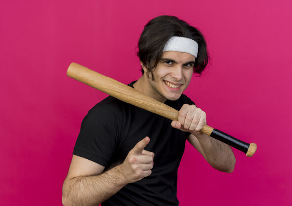 运动年轻的运动型男子穿着运动服 头戴棒球棒 用食指指着镜头 自信地微笑着食指抱着球棒