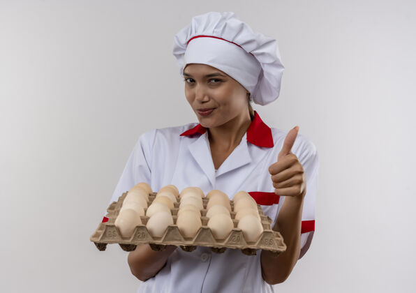 拇指高兴的年轻厨师女穿着厨师制服拿着一批鸡蛋她大拇指上孤立的白色墙壁抱厨师厨师