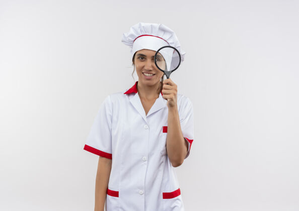 年轻年轻的女厨师穿着厨师制服拿着放大镜站在隔离的白色墙壁上 留着复印空间制服厨师厨师