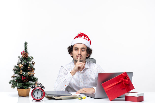 人满足忙碌自豪的年轻商人与有趣的圣诞老人帽子庆祝圣诞节 并在白色背景的办公室沉默的姿态庆祝笔记本电脑年轻的商人