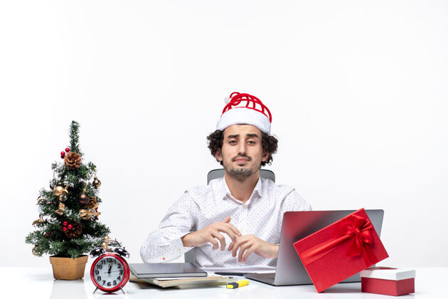 成年人忙碌的年轻商人戴着滑稽的圣诞老人帽子 在白色背景的办公室里摆姿势拍照圣诞老人年轻商人工作