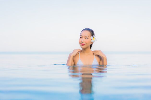 放松肖像美丽的亚洲年轻女子放松微笑周围的室外游泳池在酒店度假村日光浴度假村海滩