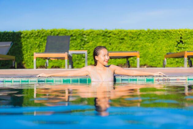 海滩美丽的亚洲年轻女子在度假酒店的室外游泳池周围放松的肖像游泳身体泳装
