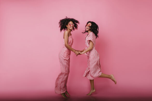 娱乐赤脚的黑发女孩一起跳舞 看着最好的朋友在粉红色衣服牵手的肖像友谊乐趣休闲