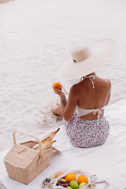 帽子一个年轻女子戴着草帽 穿着白色针织衣服坐在沙滩地毯上人奢华肖像
