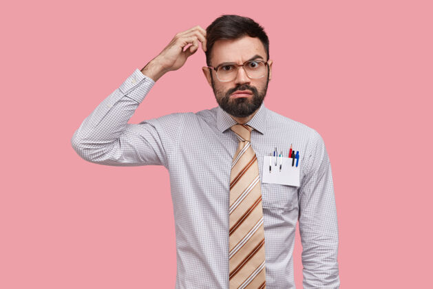 人犹豫不决的男设计师抓着头 表情严肃地看着 想着新衣服 穿着正式的衬衫 口袋里有钢笔和铅笔感觉学生态度