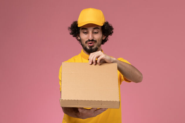 盒子正面图：身穿黄色制服的男快递员拿着食品快递箱站在浅粉色的墙上人制服帽子
