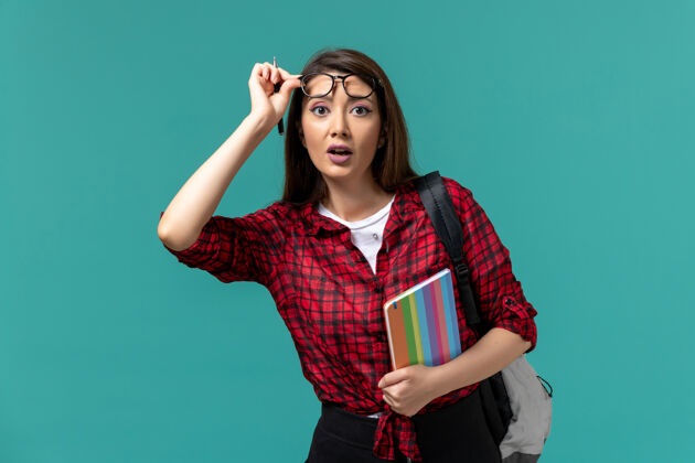 成人女学生背着书包拿着文案在蓝色墙上的正面图正面学生时尚