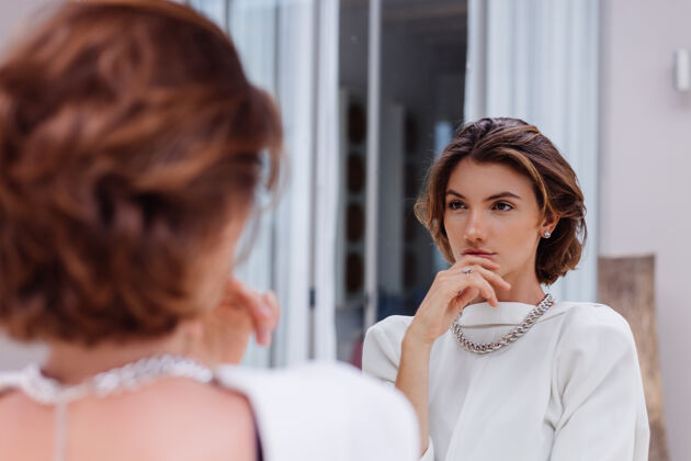 女性穿着白色西装和银色链的年轻白种女人职业模特的时尚肖像照在豪华别墅的镜子里人反射健康