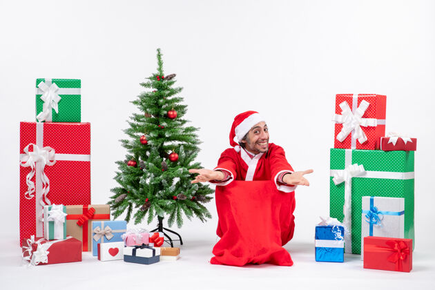 人情绪激动的年轻人打扮成圣诞老人与礼物和装饰圣诞树欢迎有人在白色背景装饰打扮礼物