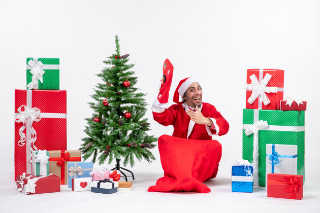 装饰新年心情与圣诞老人坐在地上 穿着圣诞袜附近的礼物和装饰圣诞树上的白色背景股票照片礼物圣诞树卖家