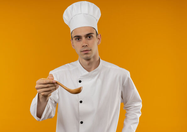 酷穿着厨师制服的年轻男性在隔离的黄色墙上伸出勺子汤匙戴着男