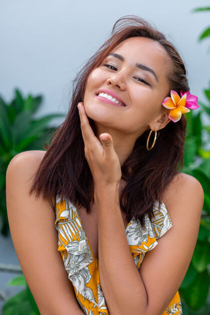 女人身着黄色夏装的亚洲女人的肖像站在那里 头发上插着泰国花 戴着圆耳环心情树叶夏天