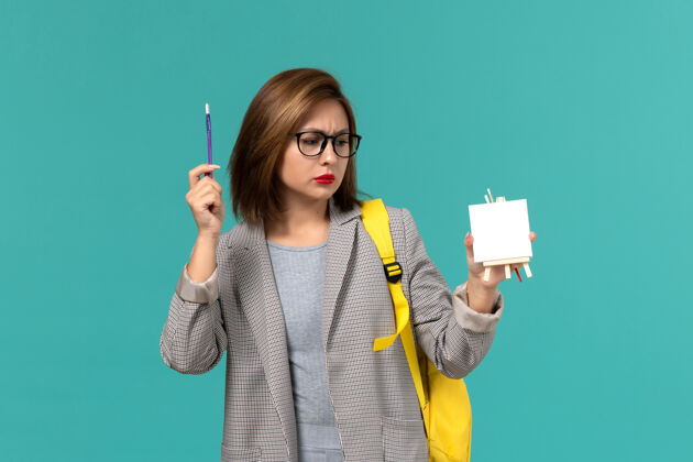 背包身着灰色夹克 黄色背包 手持流苏和浅蓝墙上画架的女学生正面图举行人画架