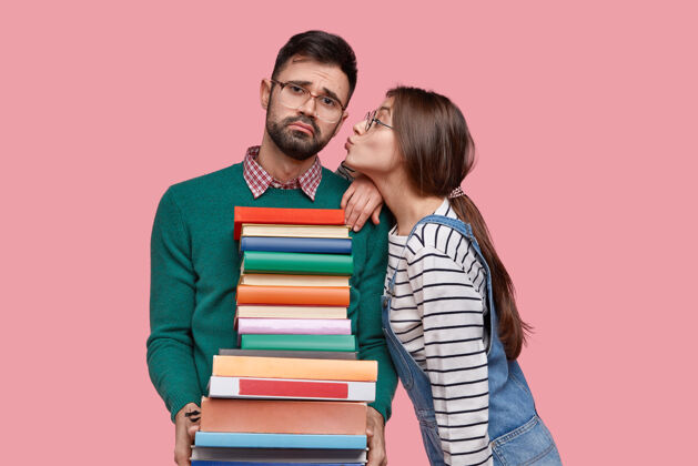 负面不高兴的没刮胡子的男人拿着课本 接吻 戴着眼镜 孤立在粉色空间的照片学生不满不高兴