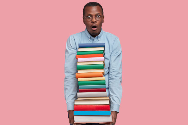 文学惊讶的非裔美国男子背着一堆五颜六色的书 害怕有最后期限 穿着正装 垂头丧气惊讶个人教科书