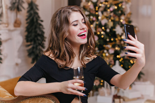 模特喜庆的女人用手机和朋友们通过视频通话 手里拿着一杯葡萄酒圣诞气氛中快乐的欧洲模特的画像人圣诞节欧洲